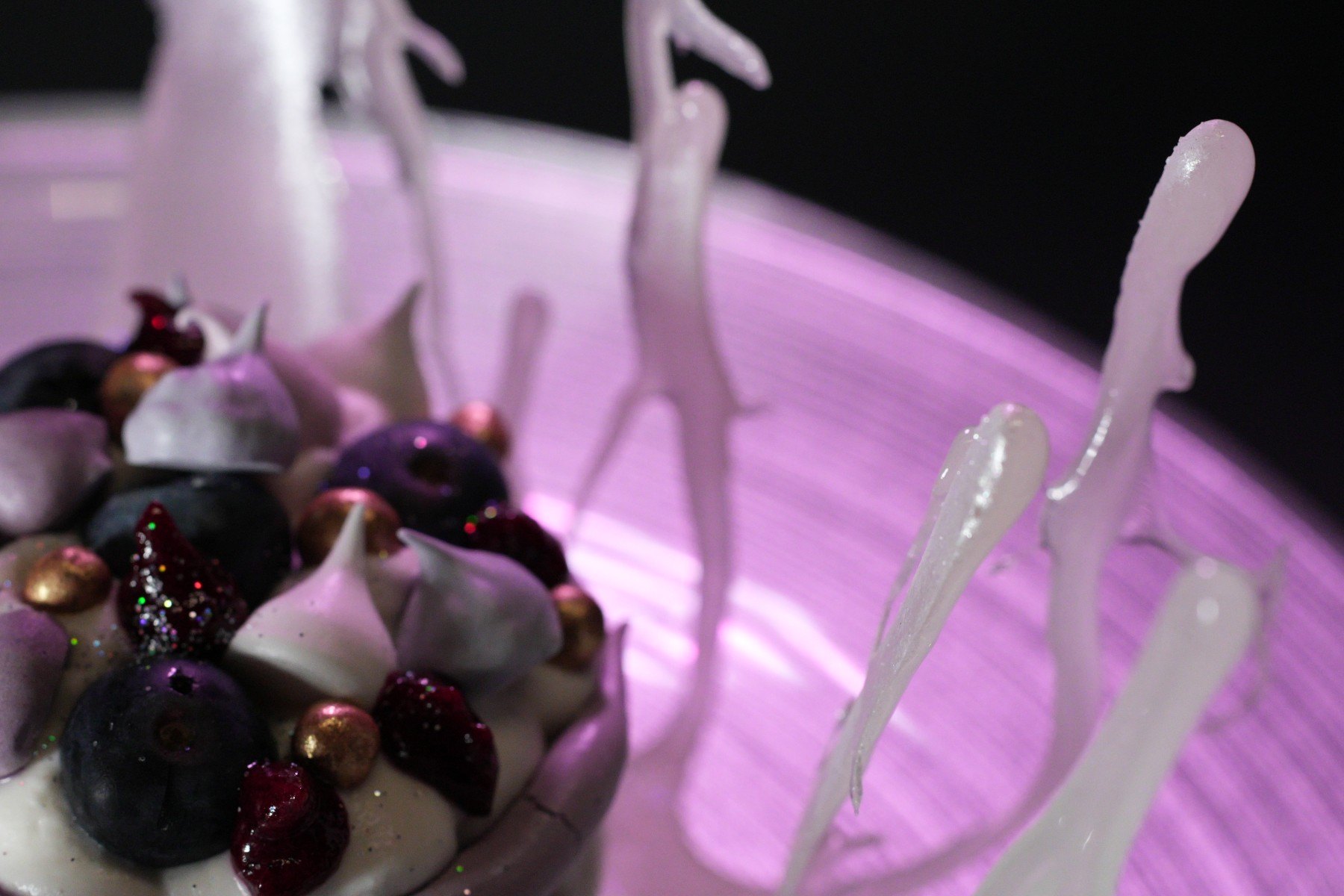 Macro frame of a berry dessert with spun-sugar shards on a glowing pink plate